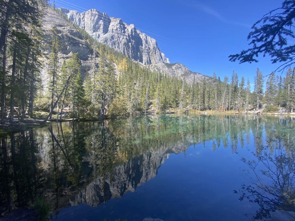 Calm Grassi Lake Kananaskis in summer with sky reflection, with trees and mountains at the back