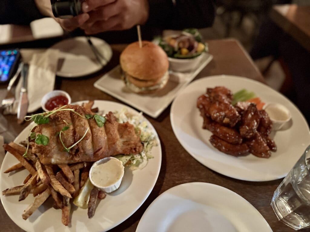 Hearty pub-style meal at Tavern 1883 in Canmore, Alberta, featuring crispy fish and chips, saucy chicken wings with ranch dip, and a gourmet burger with salad. Generous portions and great comfort food at a popular local restaurant in the Canadian Rockies.