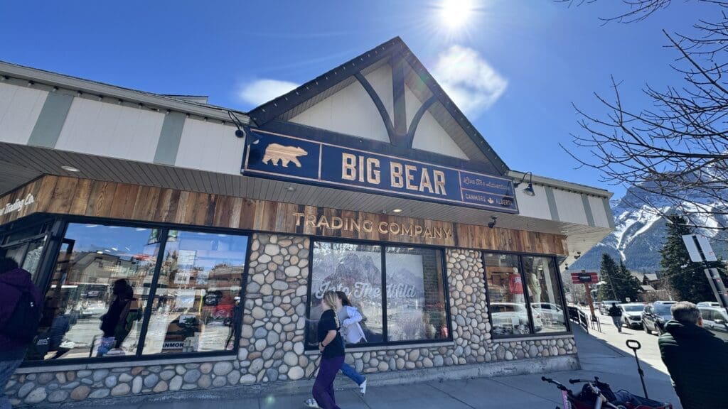 Exterior view of Big Bear Trading Company in Canmore, Alberta, with rustic wood and stone facade, offering outdoor apparel and adventure gear against a backdrop of Rocky Mountains
