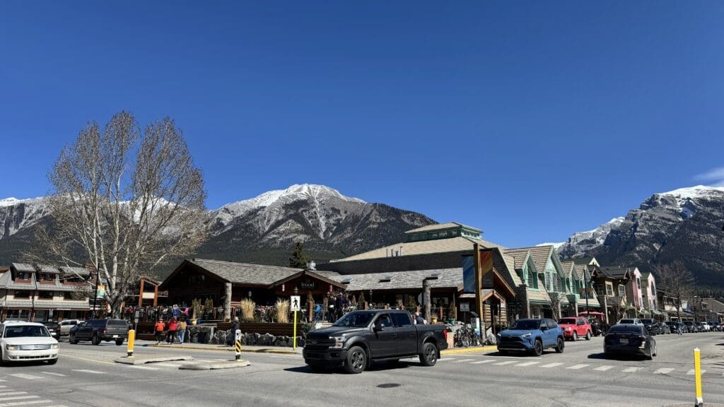 Scenic view of Main Street in downtown Canmore, Alberta, featuring local shops, restaurants, and mountain peaks in the background on a sunny day