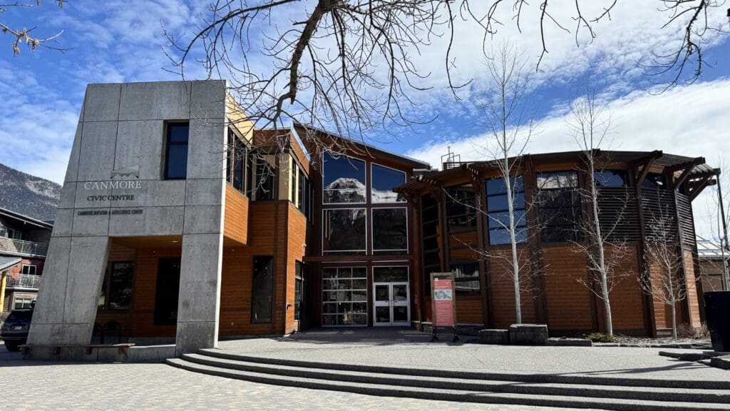 Front view of the Canmore Museum and Geoscience Centre located in the Canmore Civic Centre, featuring modern wood and concrete architecture with mountain reflections in large glass windows