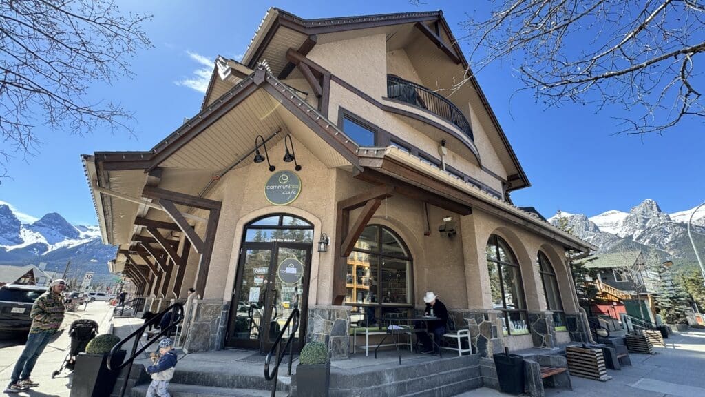 Charming exterior of Communitea Café in Canmore, Alberta with views of the Three Sisters mountains in the background and a cozy patio seating area