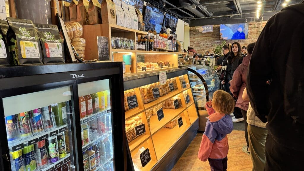 Interior view of Rocky Mountain Bagel Co. in Canmore, Alberta, showcasing a variety of fresh bagels, local pastries, and organic beverages with customers lining up at the cozy, rustic-style café.
