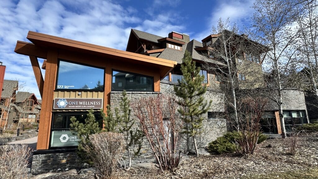 Exterior of One Wellness at Solara Resort & Spa in Canmore, Alberta, featuring rustic mountain lodge architecture with stone and wood accents on a sunny day