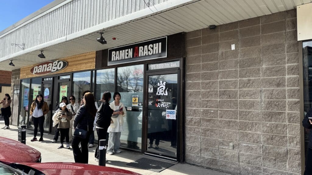 Front entrance of Ramen Arashi in Canmore, Alberta, with a small crowd of customers waiting outside, located next to Panago Pizza on 7th Avenue.