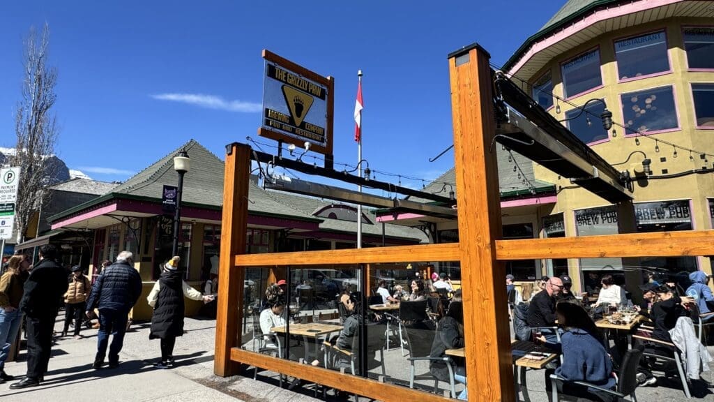 Outdoor patio at The Grizzly Paw Brewing Company in Canmore, Alberta, with customers enjoying craft beers and mountain views on a sunny afternoon
