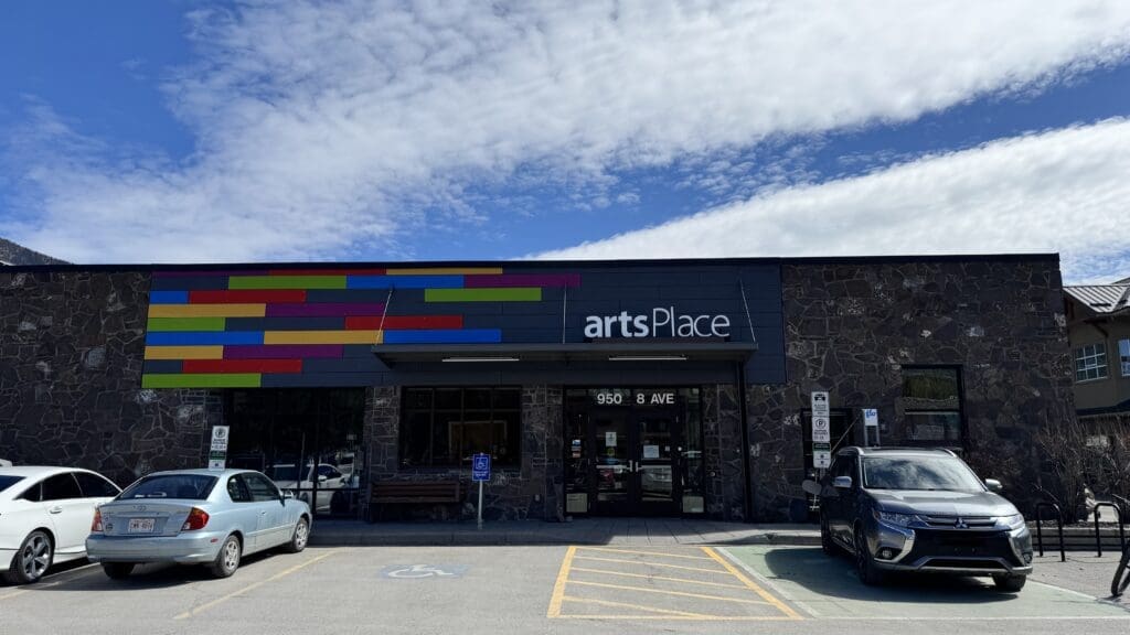 Exterior view of artsPlace Canmore, a vibrant community arts center featuring a stone facade and colorful modern signage at 950 8 Ave, with accessible parking and creative programming