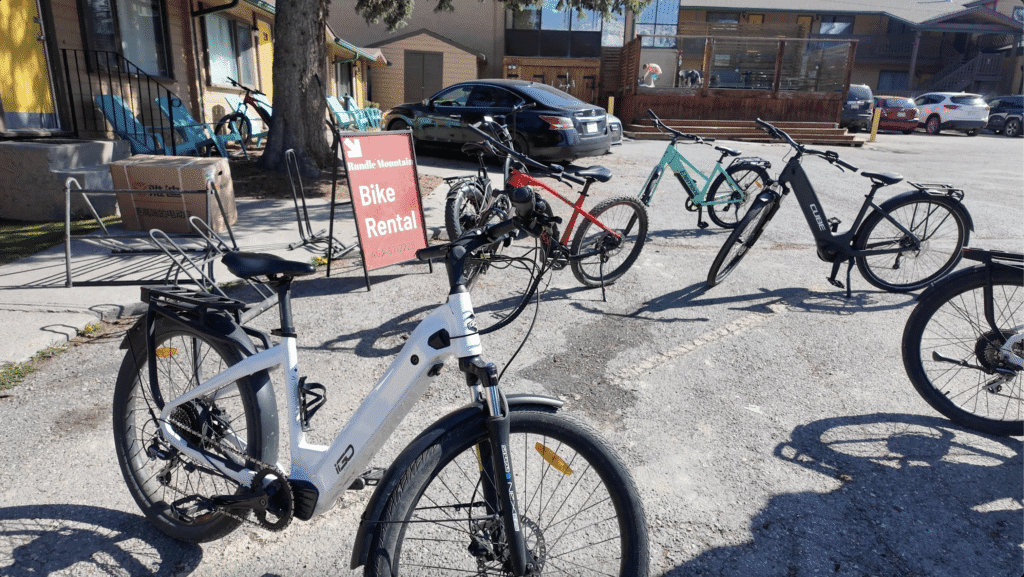 Multiple bicycles are parked near a "Bike Rental" sign in a sunny parking area in Canmore, Alberta