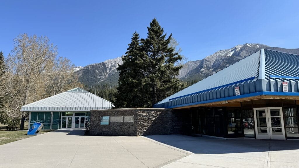 Canmore Visitor Centre in Canmore, Alberta with blue metal roofs set against a backdrop of snowy mountains and clear blue sky