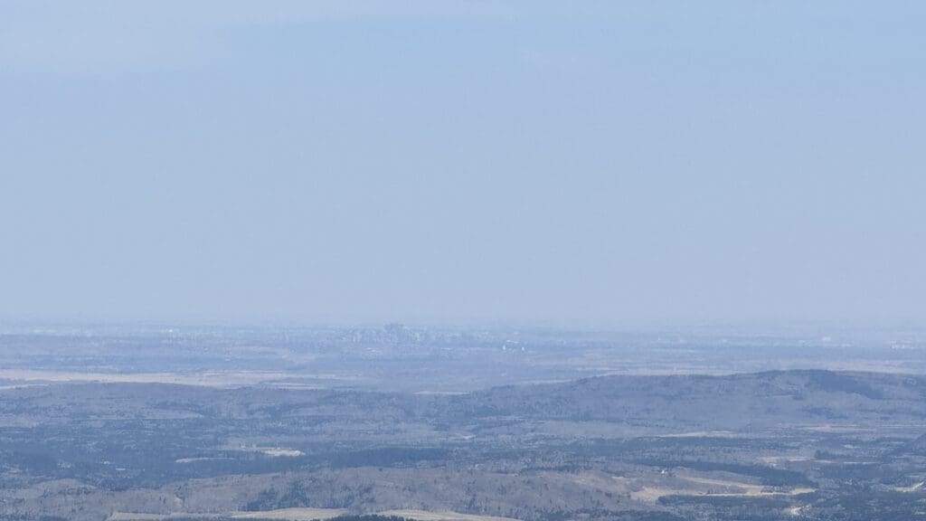 Distant city skyline of Calgary viewed from Prairie Mountain Summit in Kananaskis over a landscape of hills and valleys 