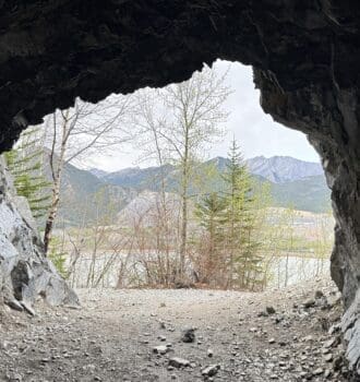 View from inside Heart Creek Bunker in Canmore, Alberta looking out at a serene landscape of trees and distant mountains under a cloudy sky