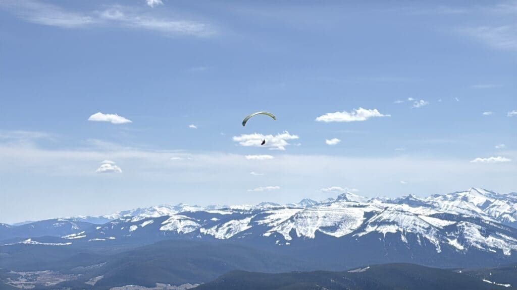Paraglider got off from Prairie Mountain in Kananaskis soaring above a snow-capped mountain range on a partly cloudy day