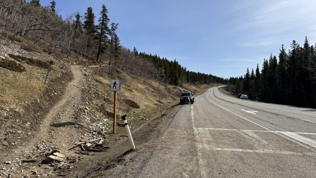 Prairie Mountain trailhead starting point with dirt path and roadside parking near forested area in Alberta