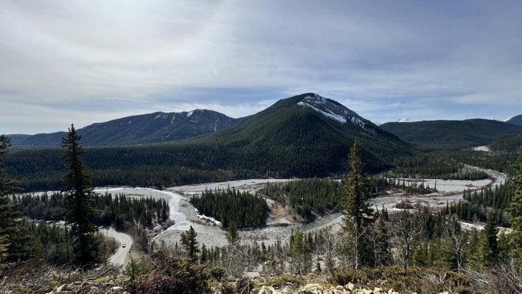 Sweeping view of Elbow River winding through forested valley below Prairie Mountain Trail with snow-capped foothills in the background