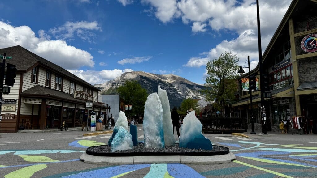 Street scene with an ice sculpture display at the center of Canmore Town, Alberta. Framed by rustic buildings, mountains, and a vivid sky, creating a vibrant, lively atmosphere.