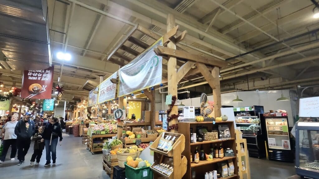 Bustling indoor Farmer's Market in Calgary, Alberta with fresh produce, wooden stalls, and vibrant signage. Shoppers browse colorful fruits and vegetables, creating a lively, welcoming atmosphere.