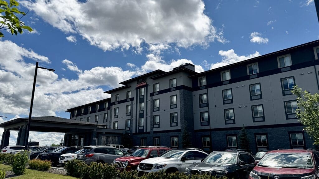 Four-story Executive Residency by Best Western in Calgary, Alberta exterior with modern design, surrounded by parked cars under a bright blue sky. Puffy white clouds add a serene backdrop.