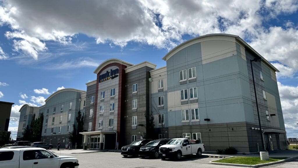 Modern four-story Park Inn by Radisson in Calgary, Alberta with an arched roof against a partly cloudy sky. Multiple cars parked in front, suggesting a welcoming and relaxed atmosphere.
