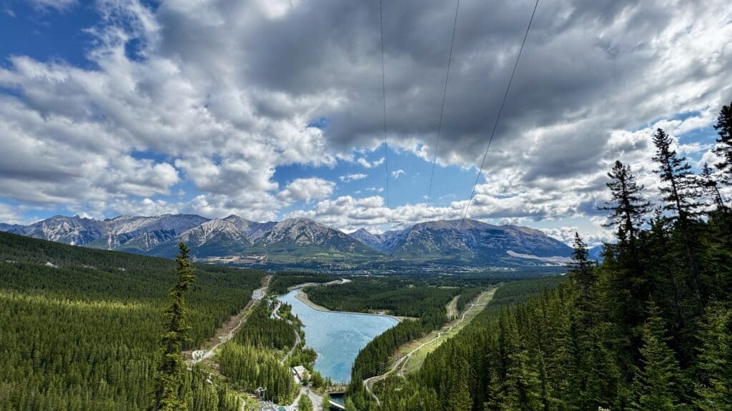 Expansive landscape view with Rundle Forebay in Kananaskis, Alberta, dense green forest, and rugged mountains under a partly cloudy sky