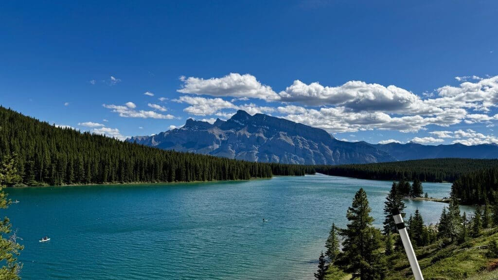 Scenic view of Two Jack Lake in Banff National Park, Alberta surrounded by dense evergreen forests, with majestic Mount Rundle under a clear blue sky and scattered clouds. Peaceful and serene.