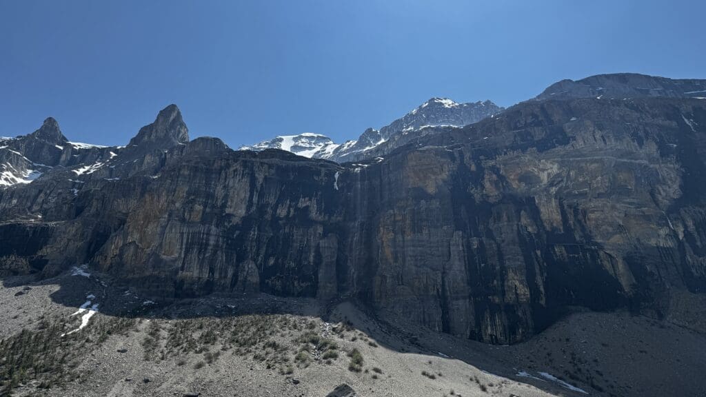 Rocky mountain landscape with snow patches under a clear blue sky, featuring sheer cliffs and sharp peaks in Stanley Glacier Trail in Kootenay National Park, BC. The scene conveys a sense of grandeur and solitude.