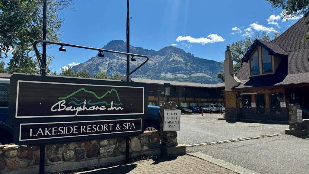 Sign for "Bayshore Inn Lakeside Resort & Spa" in Waterton Townsite, Alberta with a mountainous backdrop. Clear sky, cozy rustic buildings, and a relaxed, inviting atmosphere.