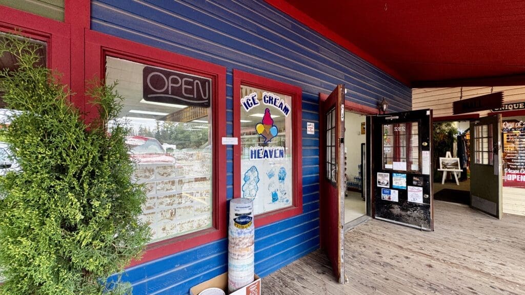 Storefront of "Ice Cream Heaven" in Bragg Creek, Alberta with vibrant blue and red trim. Glass door open, welcoming atmosphere. Potted plant and colorful mural add charm.