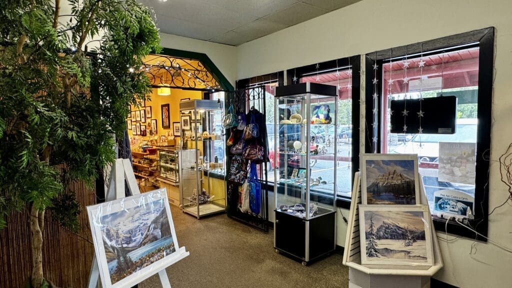 Art gallery interior in Bragg Creek, Alberta with framed paintings and crafts on display. Bright lighting, large windows with star decorations, and a calm, inviting atmosphere.
