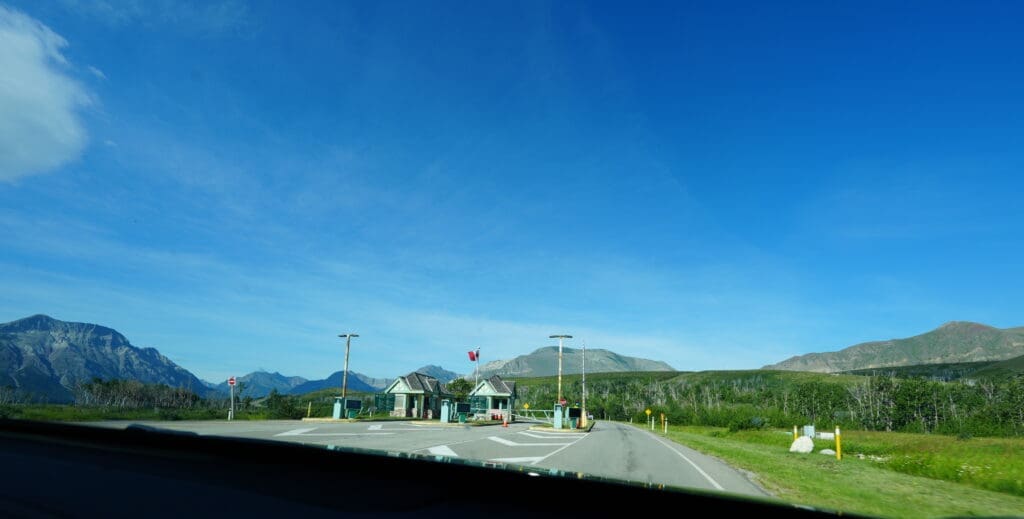 A road leads to a park gate in Waterton Lakes National Park, Alberta under a clear blue sky. Mountains form the backdrop, creating a serene and expansive landscape.