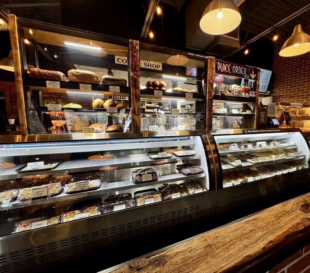 The Bragg Creek Bakery, Alberta counter displays a variety of breads, pastries, and desserts in glass cases. Warm lighting and handwritten signs create an inviting atmosphere.