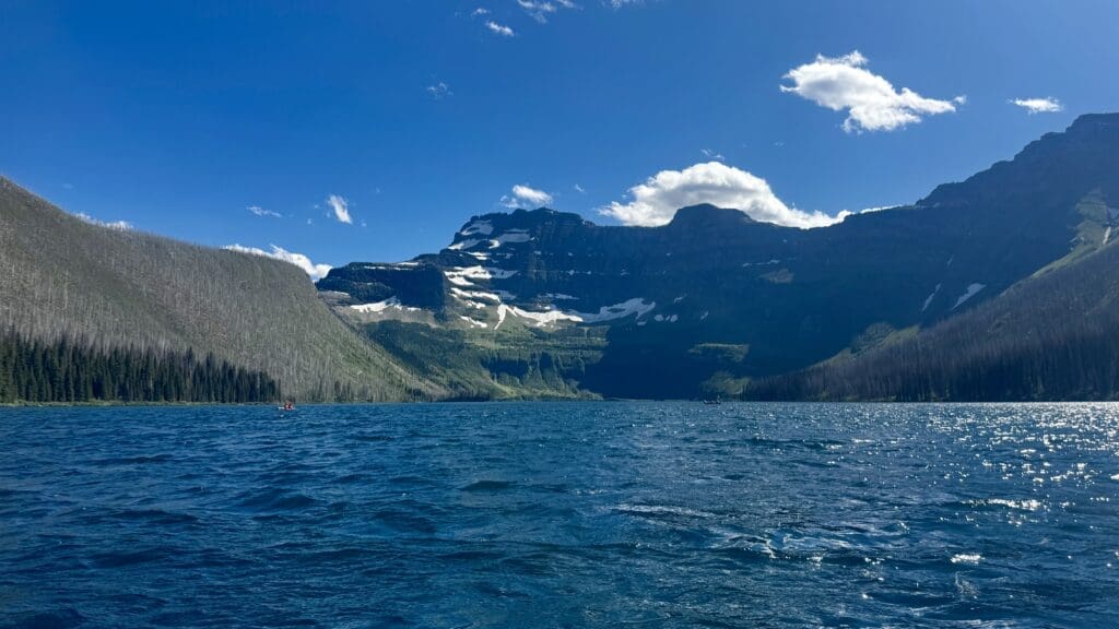A serene mountain Cameron Lake in Waterton Lakes National Park, Alberta with rippling blue water under a clear sky. Snow-capped peaks rise in the background, evoking tranquility and grandeur.