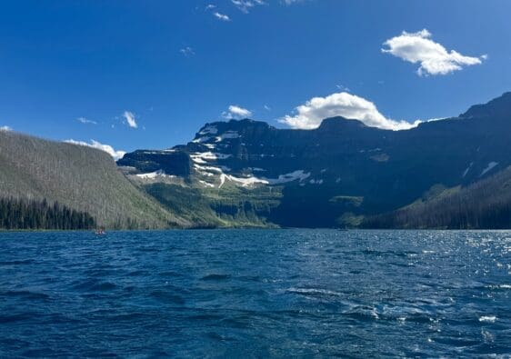 A serene mountain Cameron Lake in Waterton Lakes National Park, Alberta with rippling blue water under a clear sky. Snow-capped peaks rise in the background, evoking tranquility and grandeur.